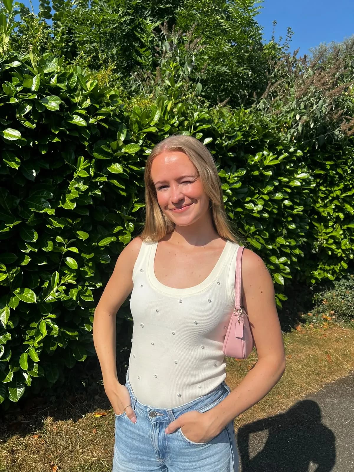 Abbie McDonnell smiling outdoors in a cream vest top with a pink shoulder bag
